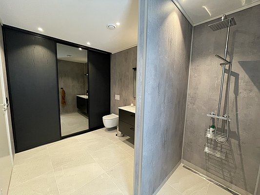 Modernes Badezimmer in Hitra, Norwegen: offene Dusche, große Spiegelfront, stilvolle graue Wände, helle Fliesen, dezente Beleuchtung. Perfekt für Angelreisende, die nach einem erfolgreichen Tag Erholung und Komfort suchen.