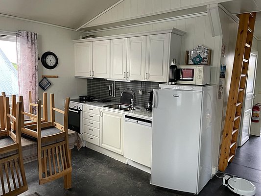 Helle, gemütliche Küche in Nordland, Norwegen, mit moderner Ausstattung. Ein großer Kühlschrank, Backofen, und Spülmaschine vorhanden. Perfekt für Erholung nach einem erfolgreichen Angeltrip. Holzleiter führt zu einem oberen Bereich.