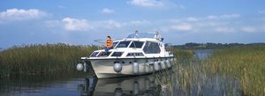 Ein modernes Hausboot gleitet sanft über den River Shannon in Irland, umgeben von hohen Schilfrohren und unter einem klaren, blauen Himmel. Perfekt für einen entspannten Angelurlaub in idyllischer Natur.
