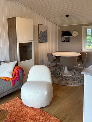 Gemütliches Wohn- und Esszimmer in Hitra, Norwegen, mit modernem Interieur: Weißer Sessel, runder Tisch, graue Stühle, Holzboden. Perfekte Unterkunft für Angelurlaub und Naturerlebnis. Ideal für entspannende Abende nach einem produktiven Angeltag.