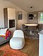 Gemütliches Wohn- und Esszimmer in Hitra, Norwegen, mit modernem Interieur: Weißer Sessel, runder Tisch, graue Stühle, Holzboden. Perfekte Unterkunft für Angelurlaub und Naturerlebnis. Ideal für entspannende Abende nach einem produktiven Angeltag.