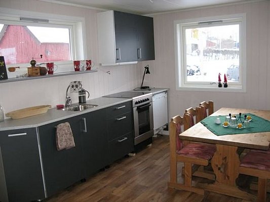 Gemütliche Küche in Nordnorwegen mit Holzfußboden, Tisch und Stühlen, modernen Geräten und großen Fenstern mit Schneeblick. Ideal für Angelurlauber, die Gemütlichkeit und Funktionalität suchen. Perfekt zur Entspannung nach einem aufregenden Angeltag.