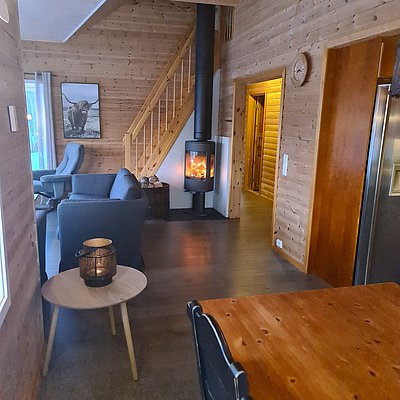 Gemütliches Interieur einer Holzhütte in Nord-Norwegen, mit knisterndem Kamin, rustikalem Mobiliar und einladendem Ambiente - ideal für Angelurlauber, die Entspannung und Abenteuer suchen.