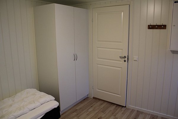Ein gemütliches Zimmer in Nord-Norwegen mit Holzfußboden, weißem Kleiderschrank und einer Tür. Ideal für Erholung nach einem ereignisreichen Angelurlaub in Norwegen. Klare, ruhige Atmosphäre.