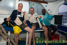 Auf einem Boot auf den Malediven sitzen drei Angler, die stolz ihre Fänge und Angelausrüstung präsentieren. Sie wirken entspannt und fröhlich, umgeben von einer maritimen Kulisse. Ideal für einen abenteuerlichen Angelurlaub.