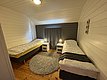 Gemütliches Schlafzimmer mit zwei Einzelbetten, Holzwänden und -boden, in Hitra, Norwegen. Ideal für Angelurlaub. Dezente Beleuchtung und neutraler Teppich schaffen eine einladende Atmosphäre für erholsame Nächte nach einem ereignisreichen Angeltag.