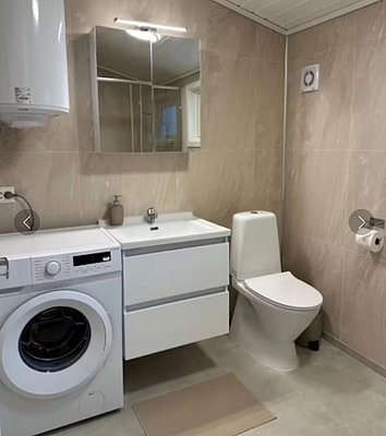 Modernes Badezimmer in Hitra, Norwegen, mit Waschmaschine, Waschbecken, Spiegel und Toilette. Helle Fliesen und saubere Ausstattung bieten Komfort für Angler während ihres Angelurlaubs. Perfekt für Erholung nach einem erfolgreichen Tag am Wasser.