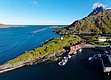 Küstenlandschaft in Nordland, Norwegen: Malerische Fjorde, ruhig gelegene Boote und traditionelle rote Holzhäuser unter klarem, blauem Himmel. Perfektes Ziel für Angelurlaub und Meeresangeln, umgeben von majestätischen Bergen und unberührter Natur.