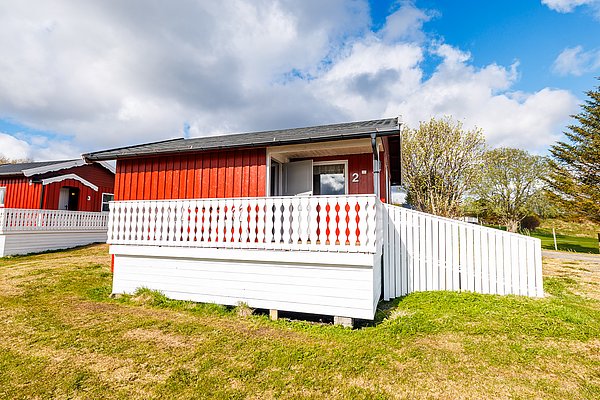 Rotes Holzhaus mit weißem Zaun auf Hitra, Norwegen. Blauer Himmel, grüne Wiese, ideal für Angelreisen und Erholung. Perfekte Unterkunft für Naturliebhaber und Angler, die das Abenteuer im skandinavischen Paradies suchen.