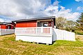 Rotes Holzhaus mit weißem Zaun auf Hitra, Norwegen. Blauer Himmel, grüne Wiese, ideal für Angelreisen und Erholung. Perfekte Unterkunft für Naturliebhaber und Angler, die das Abenteuer im skandinavischen Paradies suchen.
