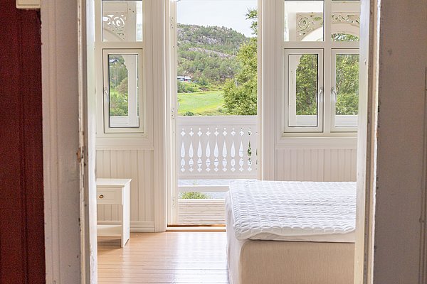 Gemütliches Schlafzimmer auf Hitra, Norwegen, mit hellen Holzelementen und Balkon, bietet friedlichen Ausblick auf grüne Landschaft. Ideal für Angelurlaub mit Entspannung in skandinavischer Natur.