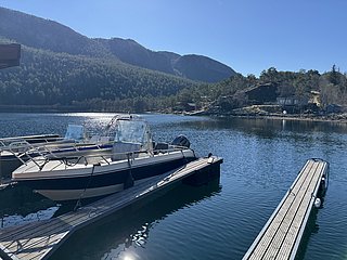 Angelboote liegen an einem ruhigen Steg, umgeben von atemberaubender Landschaft in Hitra, Norwegen. Die klare Wasseroberfläche spiegelt die üppigen Wälder und Berge wider, perfekt für einen Angelurlaub in unberührter Natur.