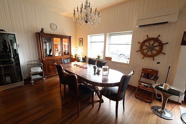 Gemütliches Wohnzimmer in Nord-Norwegen mit maritimer Dekoration. Holzvertäfelte Wände, ein großer Esstisch, hölzernes Schiffssteuerrad und ein imposanter Kronleuchter sorgen für ein warmes, einladendes Ambiente. Ideal für entspanntes Beisammensein.