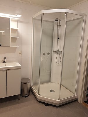 Modernes Badezimmer in Nord-Norwegen mit Duschkabine, Waschbecken und Spiegel. Helle Fliesen und funktionale Ausstattung bieten Komfort. Ideal für Erholung nach einem erfolgreichen Angelausflug. Perfekt für Angelurlaub in Skandinavien.