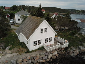 Weißes Holzhaus in Hitra, Norwegen, direkt am Ufer. Große Terrasse mit Blick auf das Wasser, umgeben von grüner Natur. Ideal für Angelurlaub und Entspannung. Atemberaubende Lage mit Zugang zum Meer.