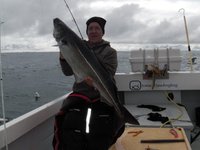 Eine Person hält einen großen Fisch auf einem Bootsdeck mit einer „Iceland Sea Angling“-Ausrüstung im Hintergrund.