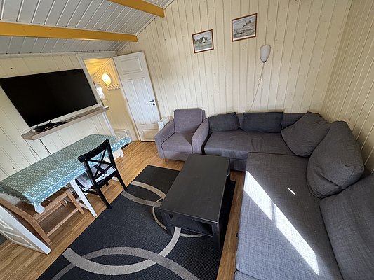 Gemütliches Wohnzimmer in Hitra, Norwegen: moderne graue Couch, eleganter Teppich, Flachbild-TV, Esstisch mit blauer Tischdecke. Idealer Rückzugsort für Entspannung nach einem erfolgreichen Angeltag. Perfekt für Angelurlauber.