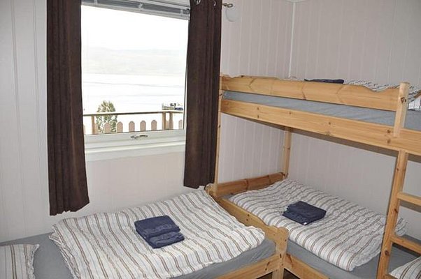 Gemütliches Schlafzimmer in Nord-Norwegen mit Etagenbetten, gestreifter Bettwäsche und Fensterblick auf Fjordlandschaft. Perfekt für Angelurlaube, bietet Komfort und Nähe zur Natur. Optimale Unterkunft für Abenteuerreisende und Angler.