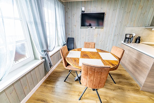 Gemütlicher Essbereich in Nord-Norwegen mit Holztisch und gepolsterten Stühlen, großen Fenstern, Fernseher und moderner Küche; idealer Rückzugsort nach einem abenteuerlichen Angeltag. Perfekte Verbindung von Komfort und Naturerlebnis.