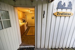 Gemütliche Trollstuo-Kabine in Nordland, Norwegen: Einladendes Kücheninterieur aus Holz mit offenem Eingang, rustikaler Atmosphäre und skandinavischem Charme. Perfekt für Angelreisen und Naturerlebnisse.