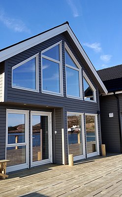 Modernes Ferienhaus in Nordland, Norwegen mit großen Fenstern und Terrasse, bietet atemberaubende Aussicht auf das Wasser und die umliegende Landschaft. Perfekt für Angler im Angelurlaub und Naturliebhaber – Entspannung und Abenteuer vereint.