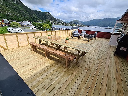 Geräumige Terrasse mit hölzernen Sitzmöbeln, Grill und atemberaubendem Blick auf Fjord und Berge in Südwest-Norwegen. Perfekt für entspannte Angelurlaube und Naturgenuss. Ideal für Gruppen und Familien.