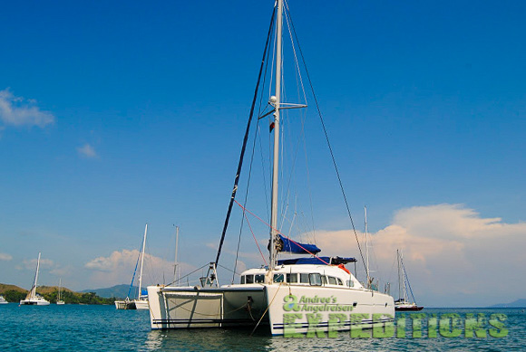 Ein weißer Katamaran namens "Andrea's Angelreisen" liegt im klaren blauen Wasser vor Anker, umgeben von mehreren anderen Segelbooten und unter einem strahlend blauen Himmel. Ein weißer Katamaran namens "Andrea's Angelreisen" liegt im klaren blauen Wasser vor Anker, umgeben von mehreren anderen Segelbooten und unter einem strahlend blauen Himmel.